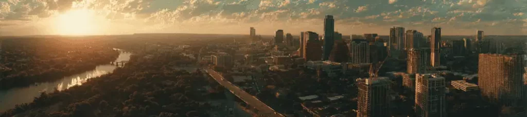 A panoramic cityscape shows downtown Austin, Texas at sunset, capturing the vibrant energy perfect for filming in Austin, with tall buildings, the Colorado River, bridges, and a sky aglow with warm golden sunlight.