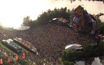 Aerial view of MYSTERYLAND, a large outdoor music festival with a dense crowd in front of an elaborate stage, nestled among trees and water, with tents and booths lining the perimeter—capturing the electric energy After the Raves.
