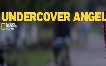 Yellow text reads UNDERCOVER ANGEL above the National Geographic Channel logo, with a blurred background of people and a street. The scene, featured in National Geographics Undercover Angel, includes a partially visible person in pink on the right.