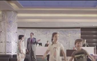 Three children are playing and smiling in the foreground of a hotel lobby, while a man in a suit and two receptionists from CTN Communications stand at the modern, marble-walled front desk.