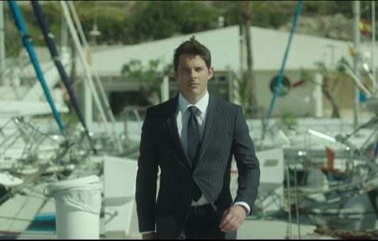 A man in a dark pinstriped HUGO BOSS suit and tie walks confidently near a marina, with boats and masts behind him—embodying the Own Your Journey spirit in this sleek commercial setting.