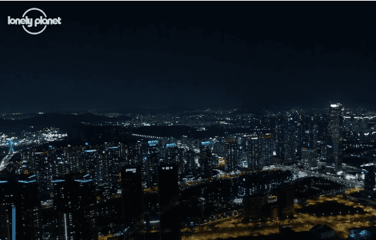 A vibrant, glowing cityscape of Incheon at night features countless illuminated buildings and streets. The Lonely Planet logo is displayed in the top left corner.