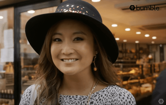 A woman wearing a black hat and patterned top smiles at the camera inside a well-lit shop, capturing Parisian picnic vibes. The Bumble logo appears in the top right corner.