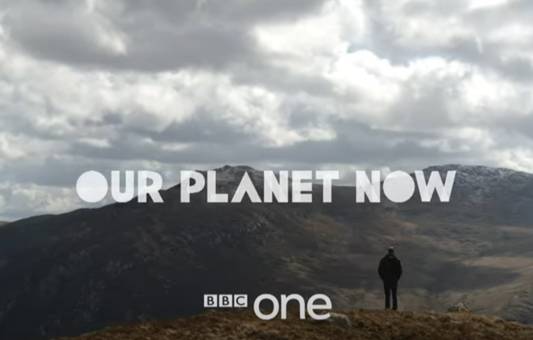A person stands on a hill overlooking mountains under a cloudy sky, representing the spirit of Repairing Our Planet, with the text OUR PLANET NOW and BBC one displayed across the scene.
