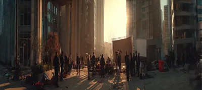 A film crew sets up equipment on a city street surrounded by tall buildings at sunset, filming in Atlanta as people stand and move around, creating a busy yet organized scene.