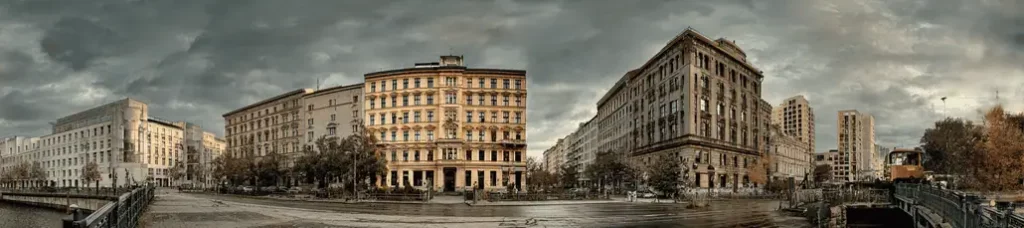 Panoramic view of historic and modern buildings along a city street under a cloudy sky, with trees and a construction vehicle in the foreground—an ideal location for filming in Berlin.