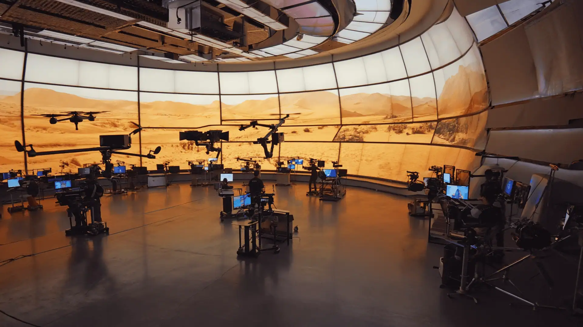 A high-tech studio with multiple camera rigs and monitors surrounds a curved wall displaying a panoramic, Mars-like desert landscape. The space has a futuristic atmosphere, seamlessly integrating best production apps with real and virtual elements.