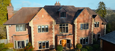 Large two-story red-brick house with multiple windows, gabled roofs, a central entrance with a wooden door, and well-kept shrubs in the front garden—perfect for a Video Production Italy project or as a set for any production company in Italy.