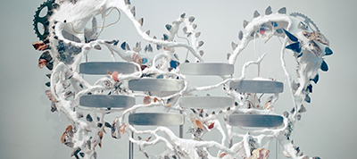 A surreal sculpture inspired by Italy features circular metal platforms, white twisting branch-like structures, gears, and scattered natural elements like leaves—perfect for a Video Production Company seeking unique visual backdrops.