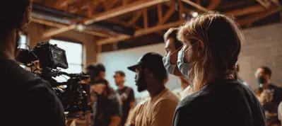 A group of people, some wearing face masks, stand indoors near a camera setup, appearing to work on a film or video production set with exposed ceiling beams—filming in Switzerland adds a unique atmosphere to the scene.