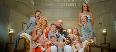 A smiling family of eight, including four children, two toddlers, and two adults, pose together on an ornate gold-trimmed sofa in a bright, elegant room—perfect for a Video Production Italy photoshoot.