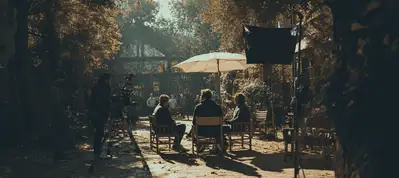 A group of people sit on chairs under a large white umbrella in a sunlit outdoor setting, surrounded by trees and film equipment, suggesting filming in Sweden is in progress.