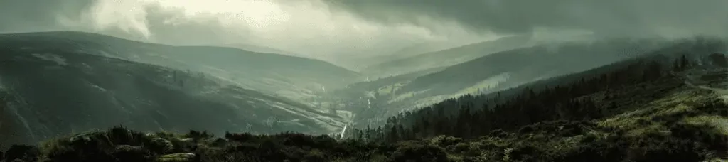 Panoramic view of misty green hills and valleys near Dublin, with a winding road, dense forests, and overcast skies creating a moody and atmospheric landscape—perfect for filming in Dublin.