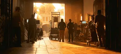 A film crew works in a large hallway with equipment and monitors, silhouetted against bright sunlight streaming in from an open doorway while filming in Chicago.