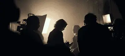 Silhouettes of several people working on a film set, dimly lit by a bright light source in the background, capture the dramatic and moody atmosphere of filming in Dublin.