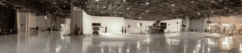 A wide view of a spacious, modern film studio in Lebanon with high ceilings, lighting equipment, cameras, and a few people setting up near a large white backdrop. The shiny floor reflects the studio lights—perfect for filming in Lebanon.