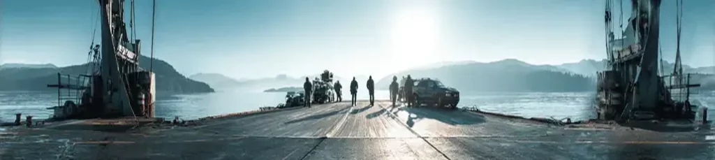 Four people and a car stand on an open ferry docked at a calm, wide body of water, with forested hills in the background and sunlight shining through misty air—evoking the magic of filming in Norway.
