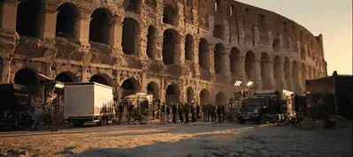A group of people filming in Rome stands in front of a historic stone building.