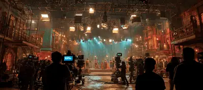 A film set with bright stage lights, cameras, and crew members captures a vibrant scene featuring actors in costume on a decorated set resembling a lively street—perfectly evoking the energy of filming in Mumbai.
