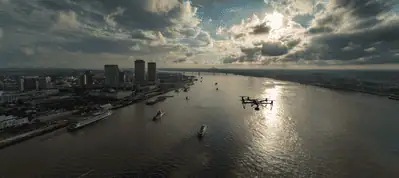 Aerial view of a river with boats and a city skyline on the left under a dramatic cloudy sky, with sunlight reflecting on the water—a stunning scene perfect for filming in New Orleans.