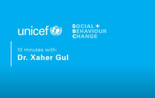 A blue graphic with the UNICEF logo and text: SOCIAL + BEHAVIOUR CHANGE. 10 minutes with: Dr. Xaher Gul in an exclusive interview.