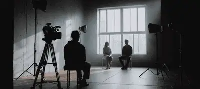 A dimly lit room with a large window, where two people sit facing a camera while a third operates filming equipment; studio lights are set up around them, capturing the dynamic atmosphere of Filming In Vietnam.