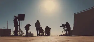 Silhouettes of a film crew filming in Israel outdoors under a bright sun, with cameras and equipment set up on a flat surface.