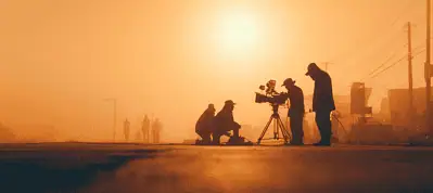 Silhouettes of a film crew setting up a camera on a street at sunrise or sunset in Turkey, with a warm orange glow in the background and a few figures walking in the distance—capturing the magic of Filming In Turkey.