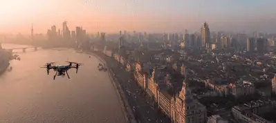 A drone flies over a wide river with a city skyline and tall buildings in the background at sunset, casting a warm, orange glow—perfect for filming in Shanghai.