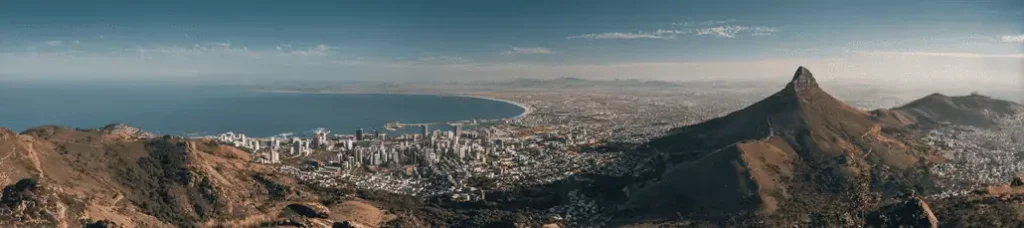 Panoramic view of a coastal city in South Africa with tall buildings, a curving bay, and a prominent mountain peak to the right under a clear blue sky—an ideal location for filming in South Africa.