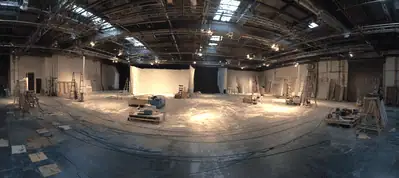 A large, empty film studio with high ceilings, industrial lighting, and scattered equipment and set pieces on the floor; tracks for cameras curve across the space—ideal for filming in Turkey.