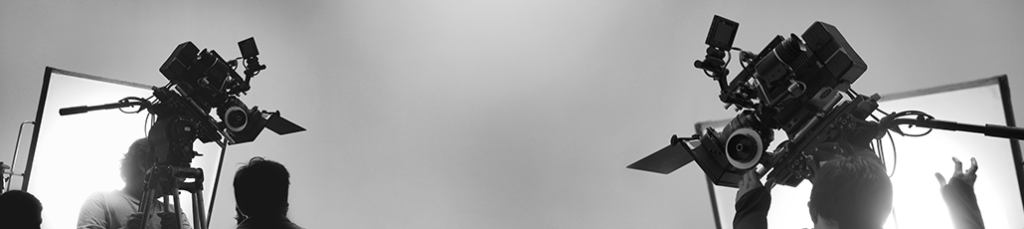 Two large film cameras on tripods face each other in a London studio, bright backlighting silhouetting people from the video production company as they work and adjust equipment in the background.