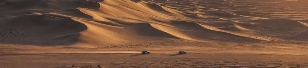 A vehicle convoy crossing desert dunes in western China.