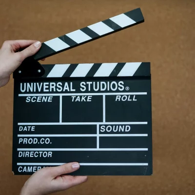 A person holds a black and white film clapperboard labeled Universal Studios against a brown background, highlighting the behind-the-scenes magic of film production services as they prepare to snap it shut.