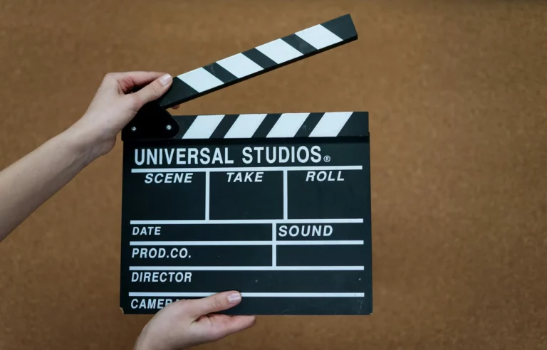 A person holds a black and white film clapperboard labeled Universal Studios against a brown background, highlighting the behind-the-scenes magic of film production services as they prepare to snap it shut.