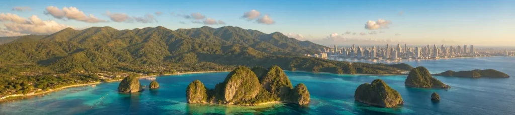 A tropical coastline, mountains and a distant city skyline in the Philippines.